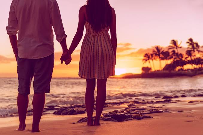 A picture of a couple standing and holding hands while viewing the sunset at a beach