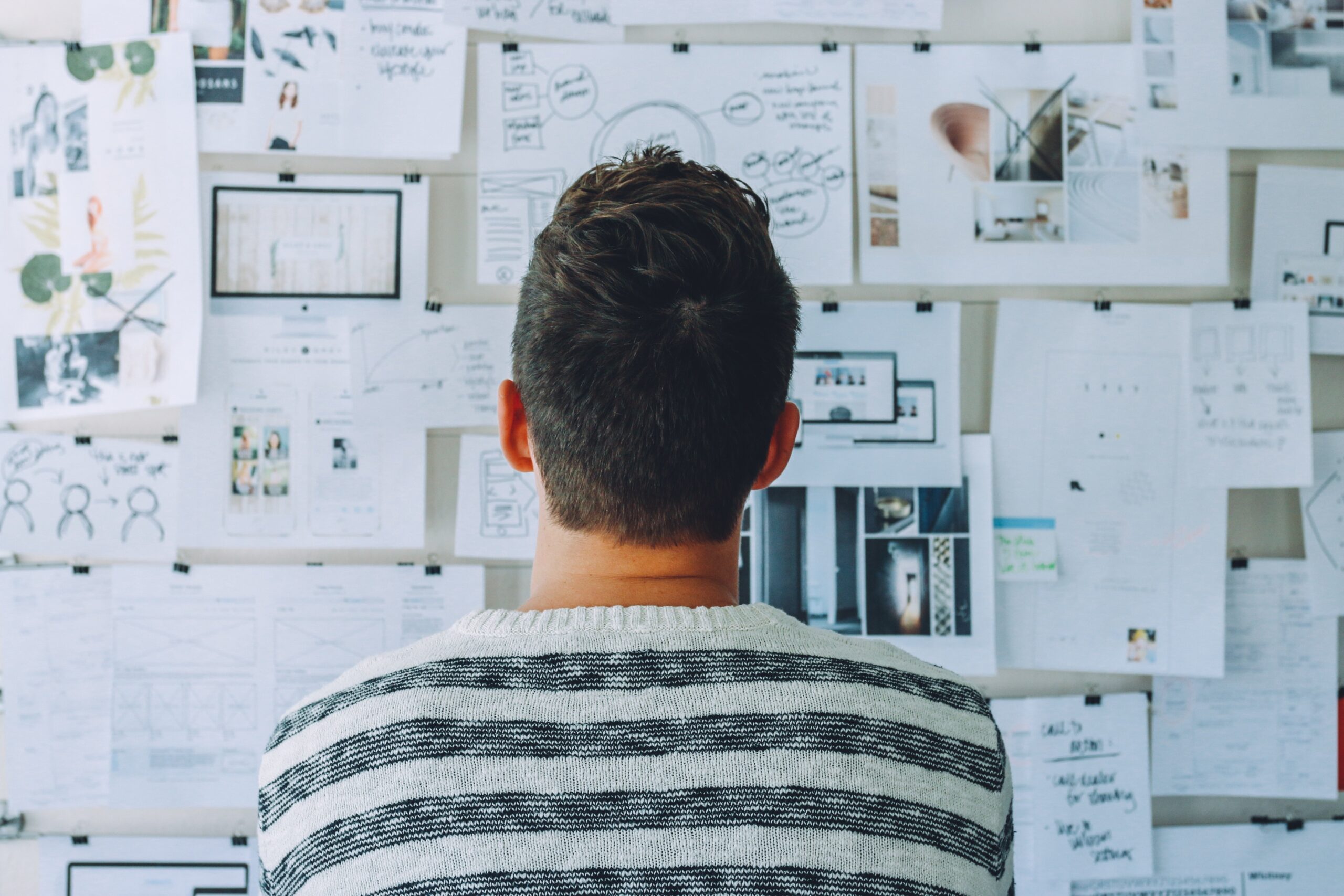 A picture of a young man looking at the plans and goals he has written down on papers and pasted on the wall